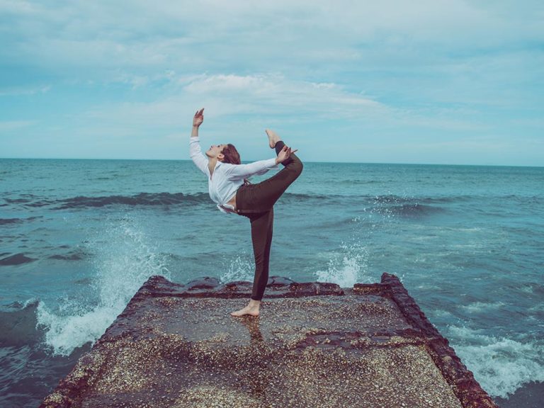 Femme en pose de yoga sur une jetée rocheuse, vagues de l'océan.