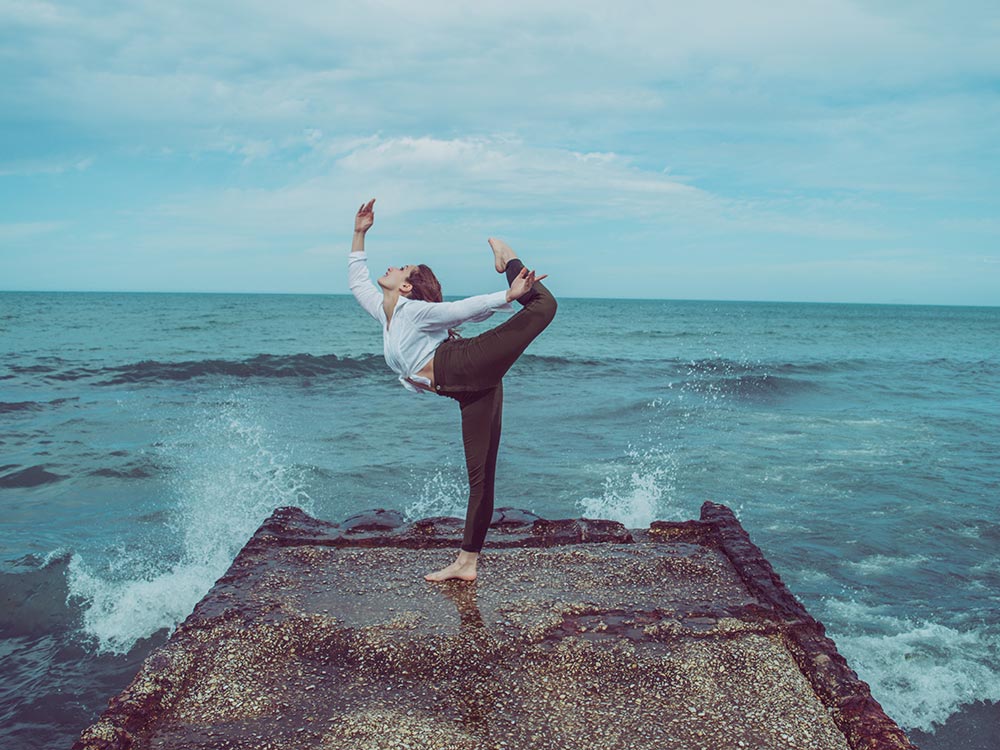 Femme en pose de yoga sur une jetée rocheuse, vagues de l'océan.