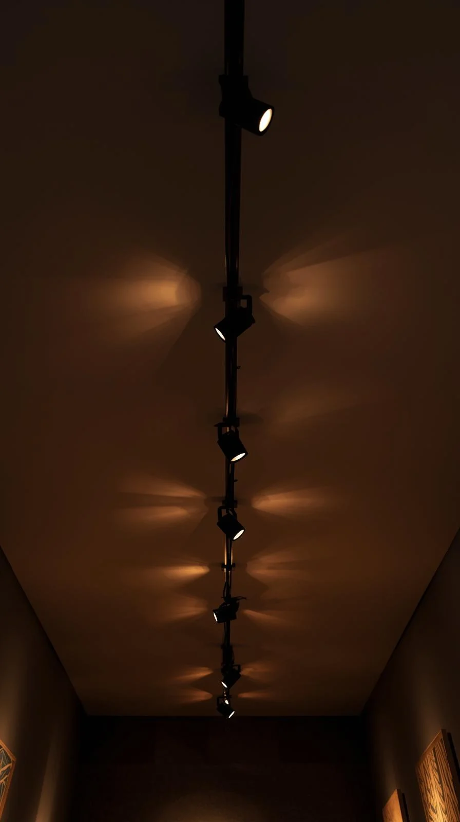 Un rail d'éclairage noir au plafond avec plusieurs spots orientables allumés, éclairant un couloir sombre.