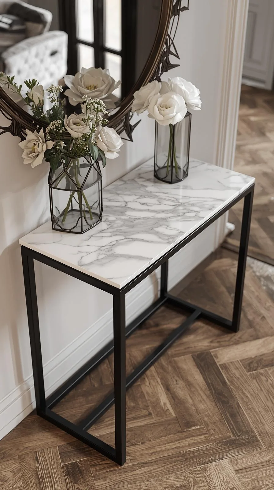 Une console d'entrée chic avec un plateau en marbre blanc veiné et une structure minimaliste en métal noir, sur un parquet.