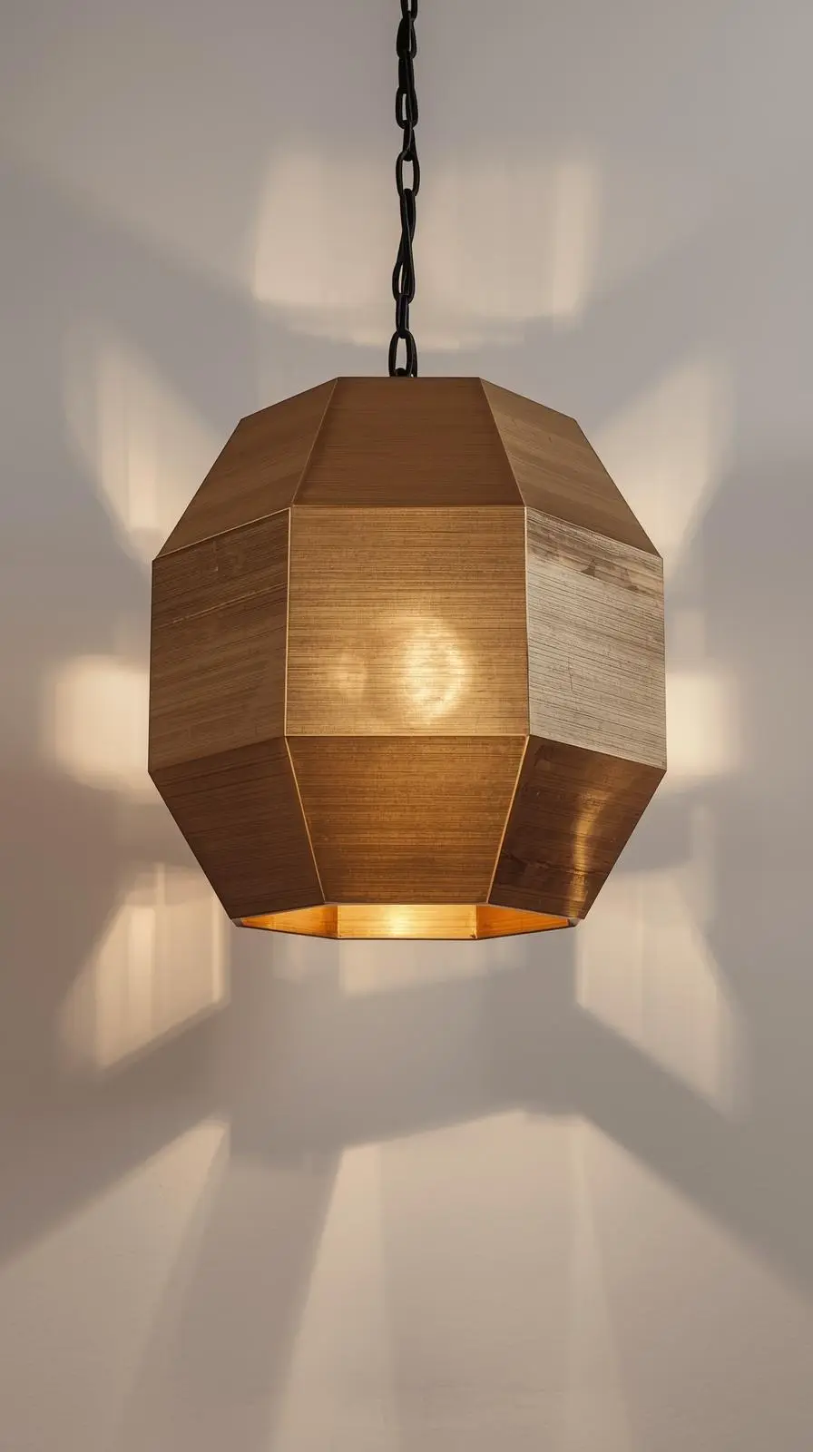 Un lustre géométrique en laiton brossé, de forme hexagonale (ou polyédrique), projetant des ombres graphiques sur un mur blanc.