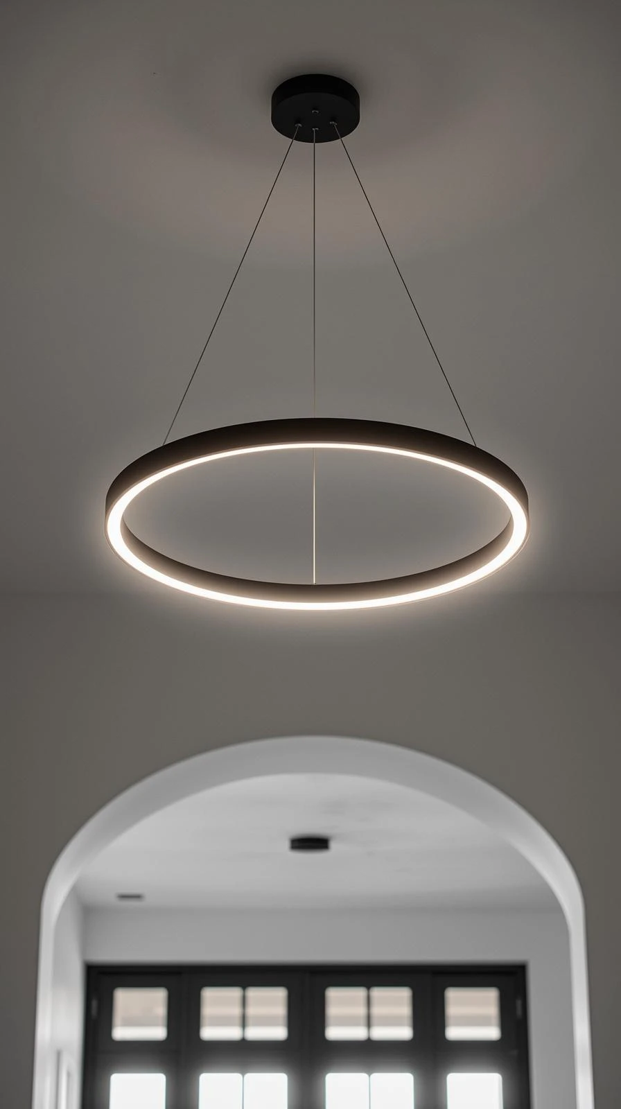 Un lustre minimaliste en forme de cercle (halo) noir mat, avec éclairage LED intégré, suspendu dans une entrée moderne avec une arche.