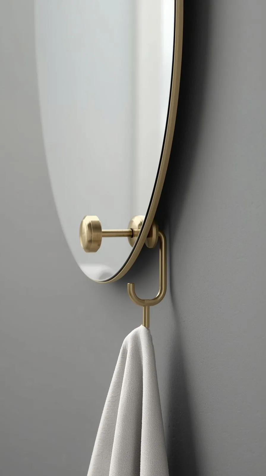 Gros plan sur le bord d'un miroir rond avec cadre en laiton, et un crochet en laiton assorti tenant une serviette grise.