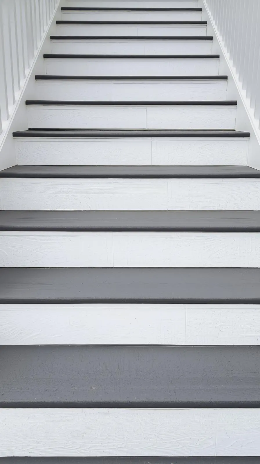 Escalier extérieur en bois peint avec des marches (girons) grises et des contremarches blanches, créant un contraste graphique.