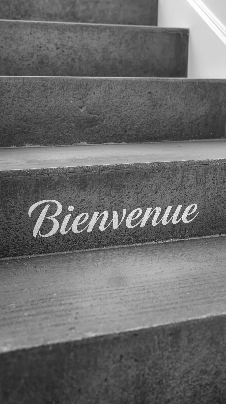 Gros plan sur une contremarche d'escalier en béton sur laquelle est écrit le mot "Bienvenue" en lettres blanches cursives.
