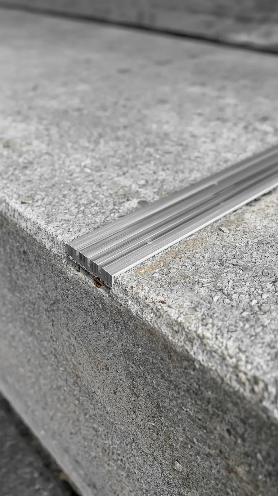 Gros plan sur le bord d'une marche en béton texturé où est fixé un profilé en métal antidérapant, aussi appelé nez de marche.