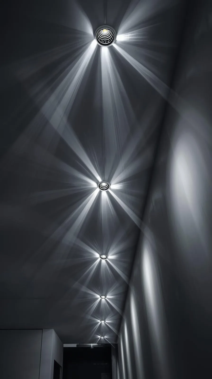 Vue en contre-plongée d'une ligne de spots LED encastrés dans un plafond sombre, créant des faisceaux lumineux graphiques et directionnels.